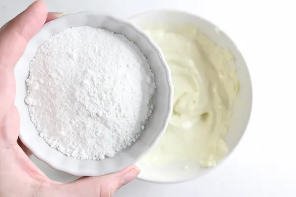 a woman's hand adding a bowl of zinc oxide powder to a bowl of homemade diaper rash cream
