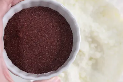 adding a bowl of hibiscus powder to a bowl of bath bomb mixture