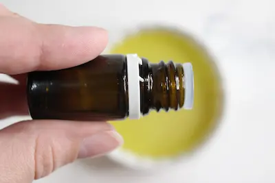 hand holding an essential oil bottle drops into a bowl of oil