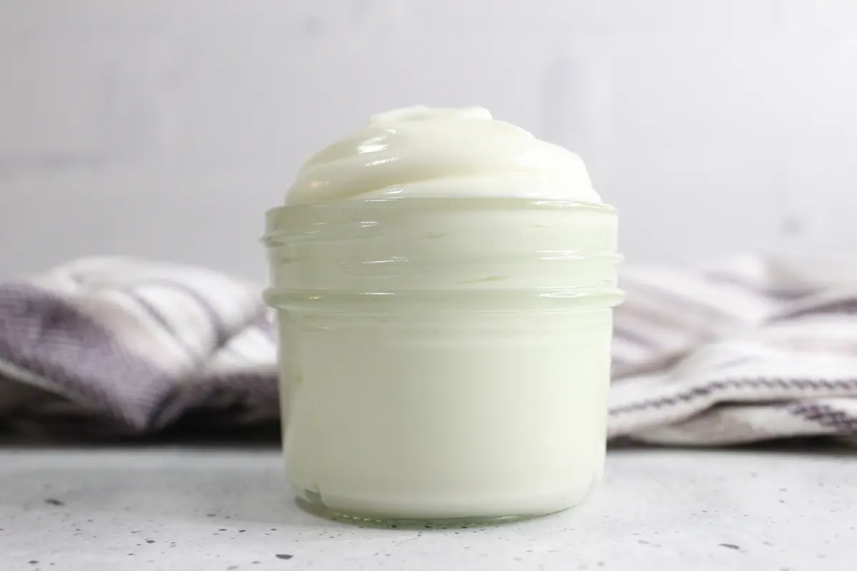 glass jar of homemade whipped tallow balm with a purple towel in the background