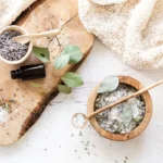 a wood bowl filled with bath salts, eucalyptus sprig, dried lavender, and a bottle of essential oil