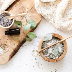 a wood bowl filled with bath salts, eucalyptus sprig, dried lavender, and a bottle of essential oil