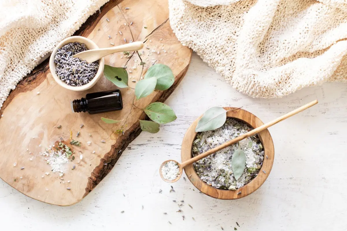 a wood bowl filled with bath salts, eucalyptus sprig, dried lavender, and a bottle of essential oil