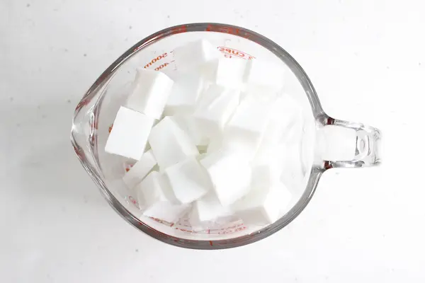 a glass measuring cup full of cut up pieces of melt and pour soap base for making tallow soap