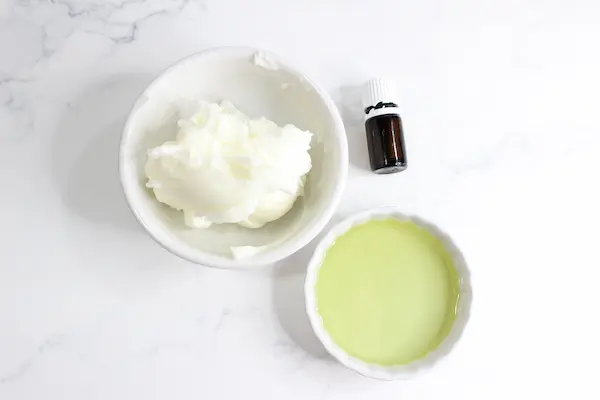 bowls of tallow balm, oil and a bottle of essential oil for making a tallow balm