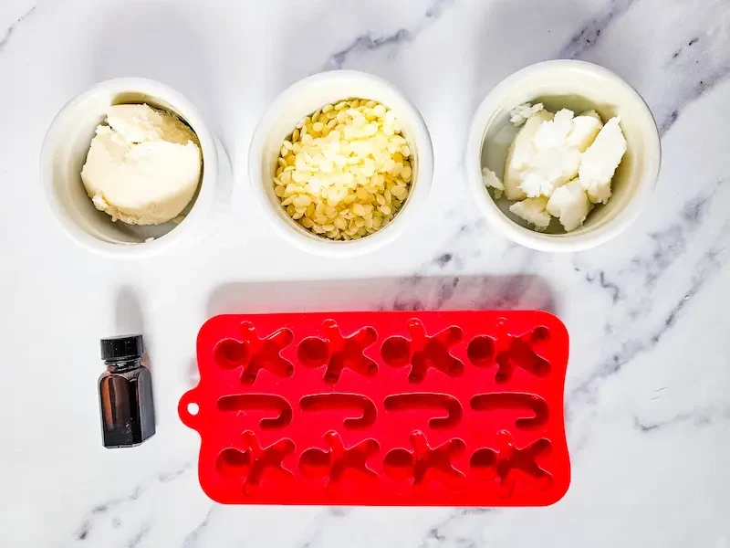 bowls of butters and oils,  bottle of essential oils, and gingerbread soap mold for making gingerbread lotion bars