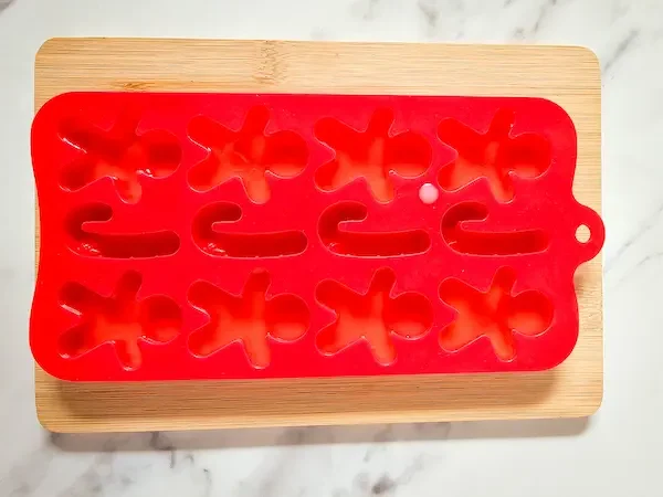 red silicone gingerbread mold on a wood cutting board filled with diy lotion bar mixture