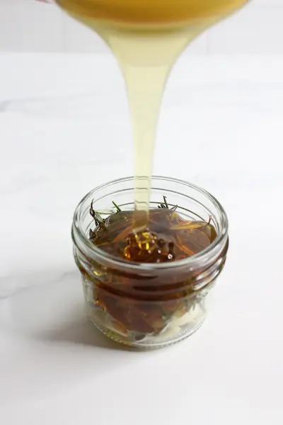 pouring honey over herbs in a jar to make infused honey