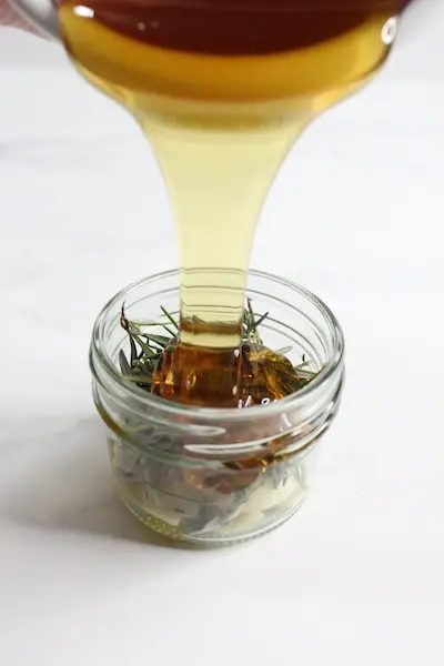 pouring honey over herbs in a jar to make infused honey