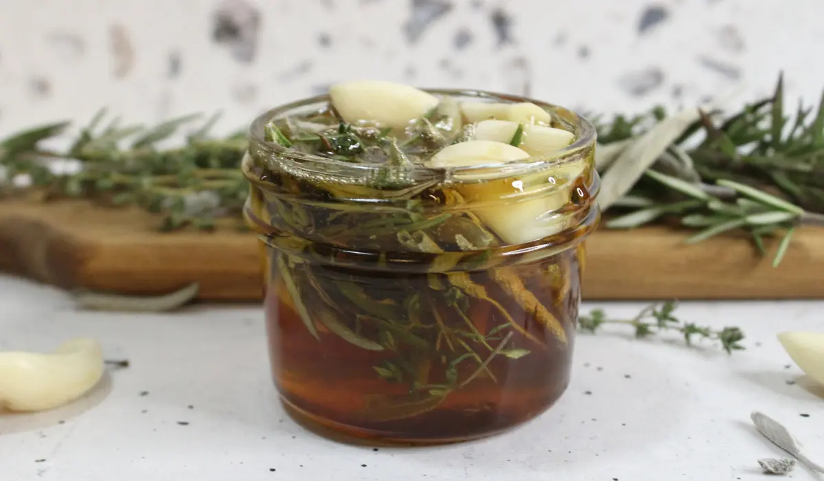 jar of homemade herb infused honey with herbs on a cutting board