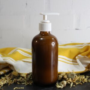 brown glass pump bottle of homemade honey calendula face wash with dried flowers