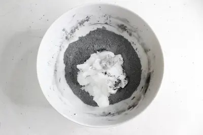 a bowl of activated charcoal powder with coconut oil on top of it for making natural toothpaste
