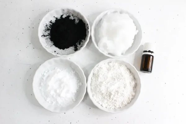 a group of bowls with activated charcoal powder and a bottle of essential oil to make natural toothpaste