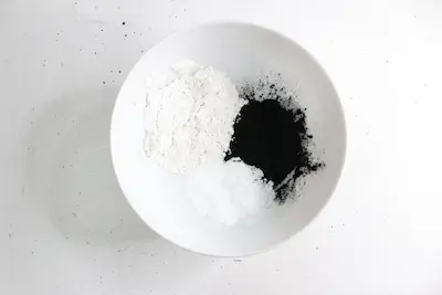 a mixing bowl with charcoal powder, and baking soda to make natural toothpaste