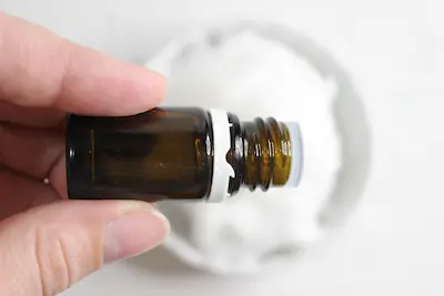 a bowl of coconut oil with a hand adding drops of essential oil to it for making natural toothpaste