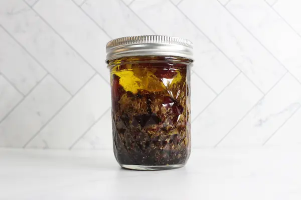 a mason jar filled with dried rose petals and carrier oil to make a rose infused oil for a diy tallow face cream