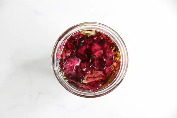 top view of a mason jar filled with dried rose petals and carrier oil to make an infused rose oil for a tallow face cream