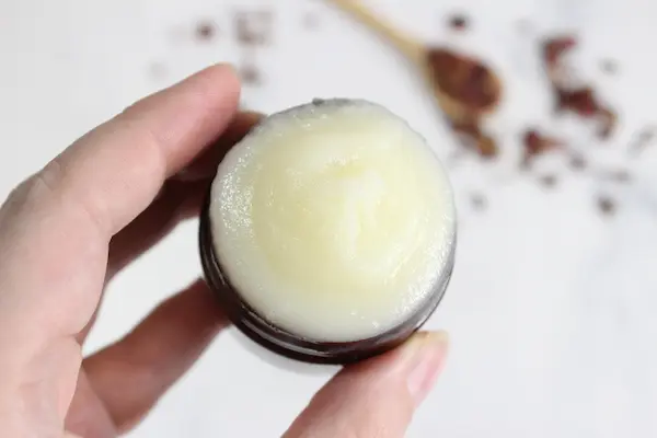 hand holding a jar of homemade fose tallow balm in a container