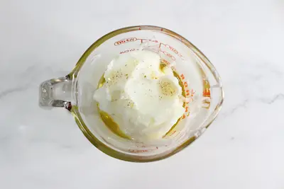 glass measuring jar filled with tallow and rose infused oil for making a face cream