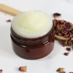 a jar of homemade rose tallow face cream with dried rose petals and a wooden spoon