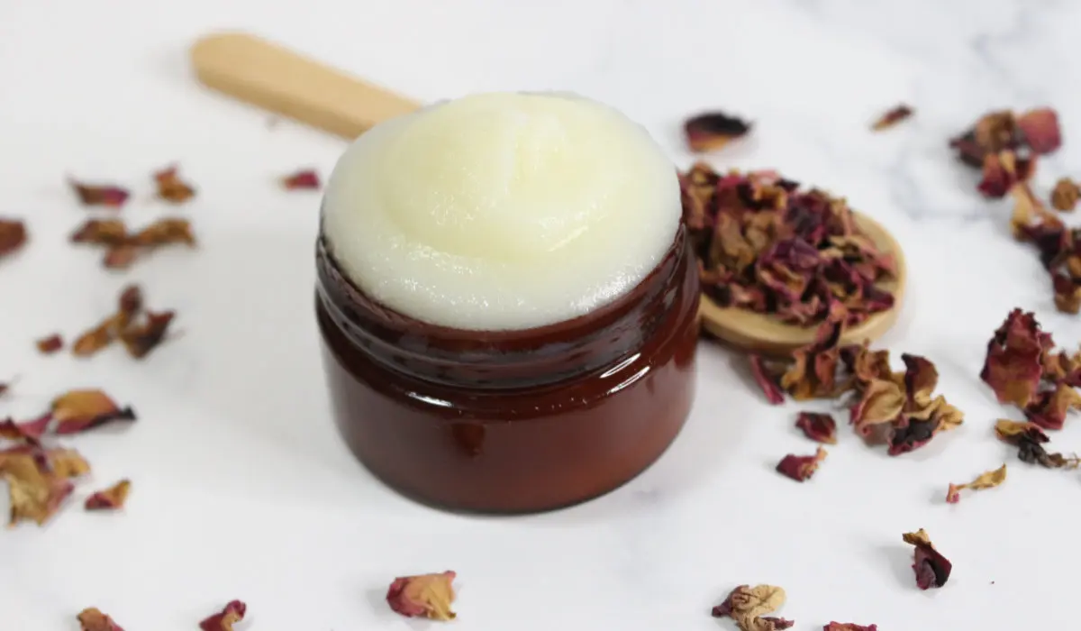 a jar of homemade rose tallow face cream with dried rose petals and a wooden spoon