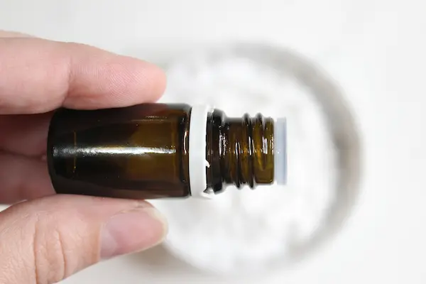 bowl of baking soda with a hand adding drops from a bottle of essential oil for making armpit detox paste
