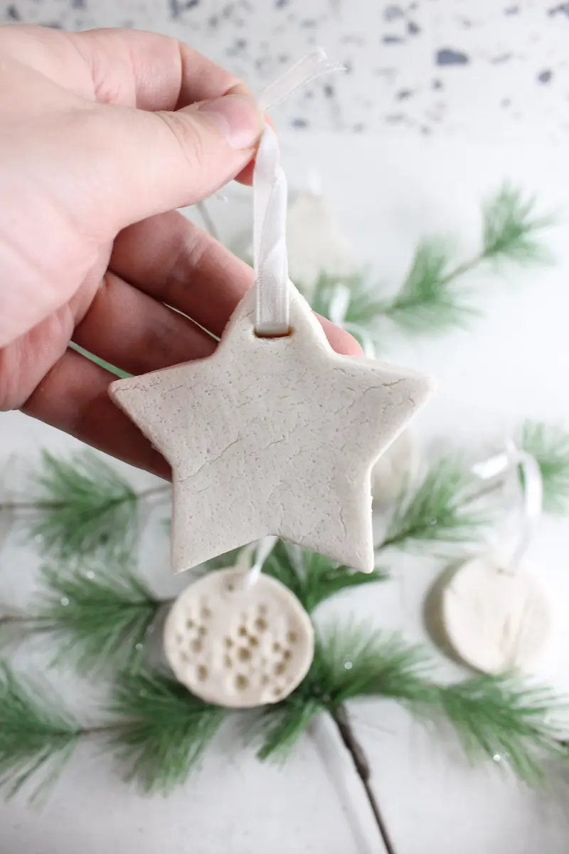 a star shaped homemade essential oil diffuser ornament being held with Christmas tree greenery in background