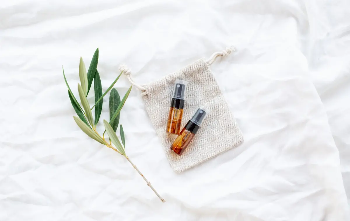 bottles of essential oil spray on white linens with a sprig of greenery