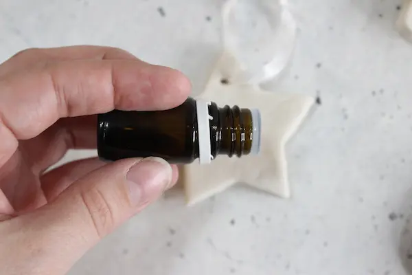 a homemade no bake diffuser ornament and a hand adding drops of essential oil to it