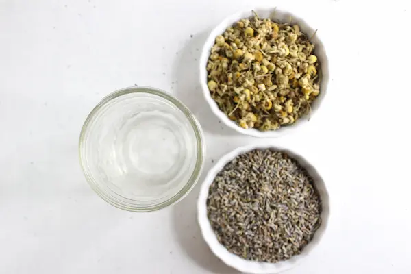 bowls of oil and dried lavender and chamomile herbs to make a homemade sleep salve