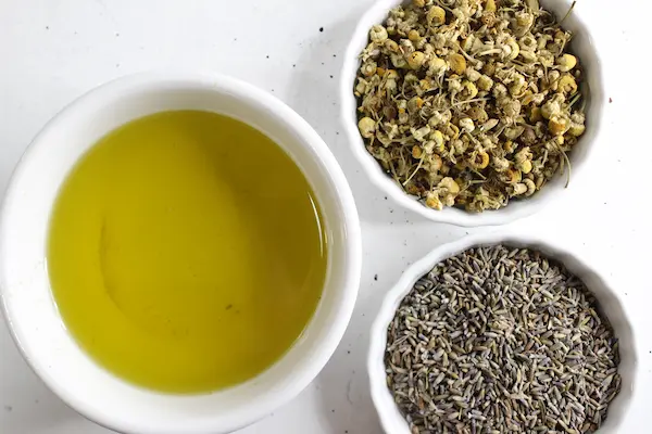 bowls of oil and dried lavender and chamomile herbs to make a homemade sleep salve