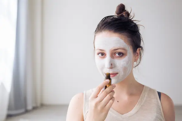 woman using a face mask and smelling a bottle of essential oil for skin care