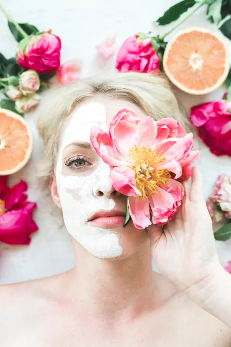 woman with a face mask, flowers, and grapefruit for natural skin care