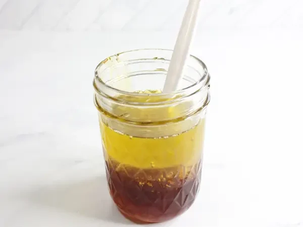 jar containing ingredients and a stir stick for making honey calendula facial cleanser