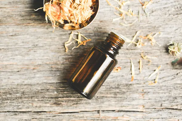a bottle of essential oil surrounded by dried calendula flowers on wood