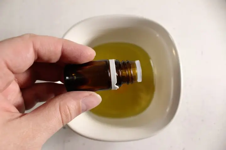 a woman's hand holding a bottle of essential oil over a bowl of oils to make diy sunscreen spray