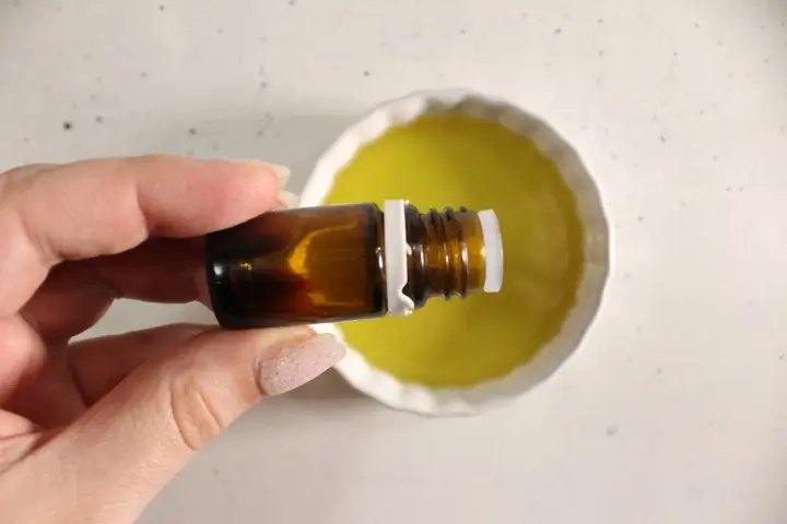 a woman's hand holding a bottle of essential oil over a bowl of carrier oil.