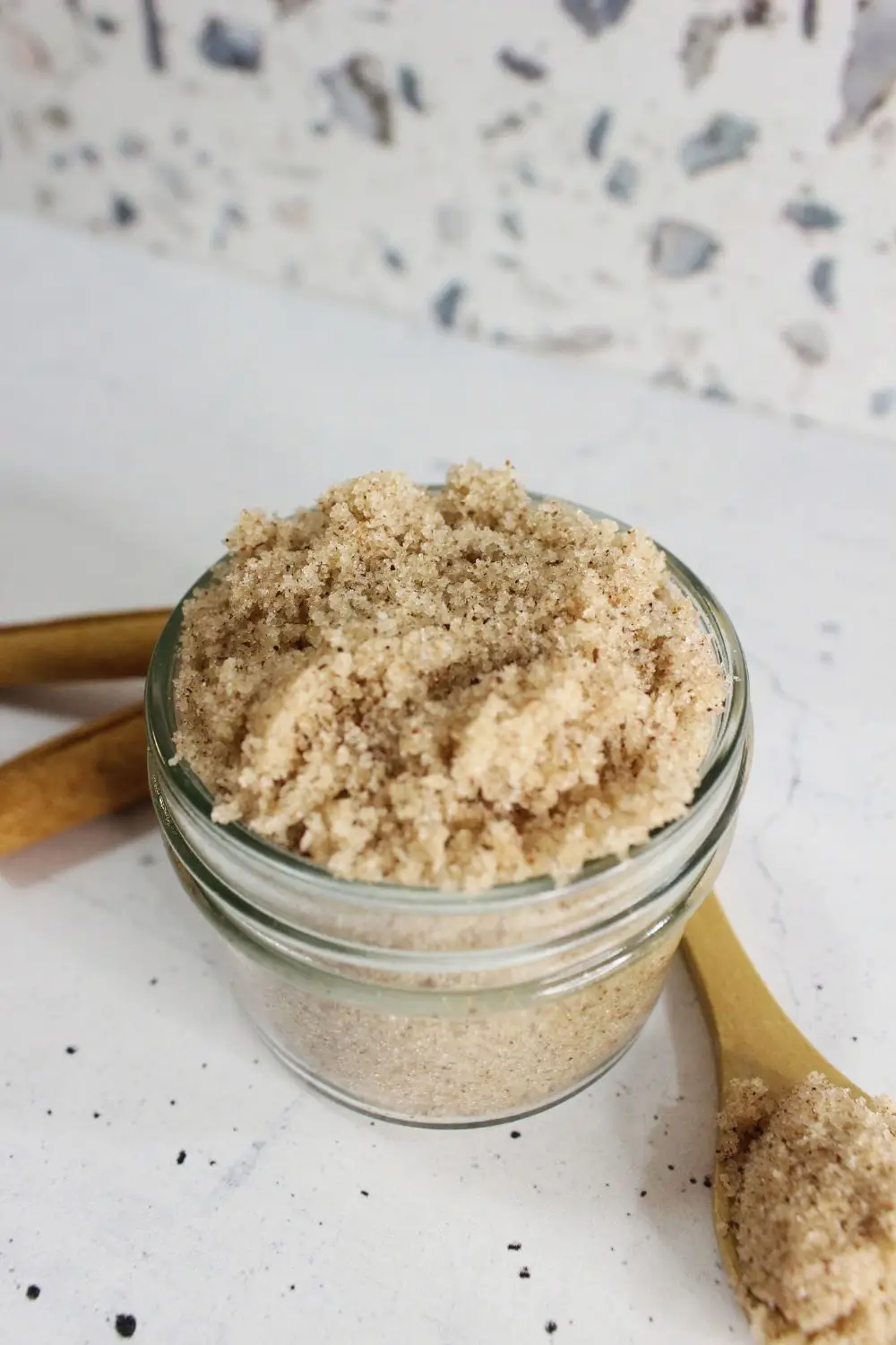 jar of homemade cinnamon sugar scrub with a wooden spoon and cinnamon sticks