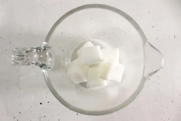 glass measuring cup with melt and pour soap base cubes in it.