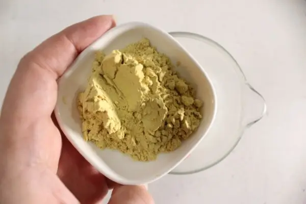 a glass measuring cup with melt and pour soap base in it and a bowl of pumpkin pie spice being added to it.