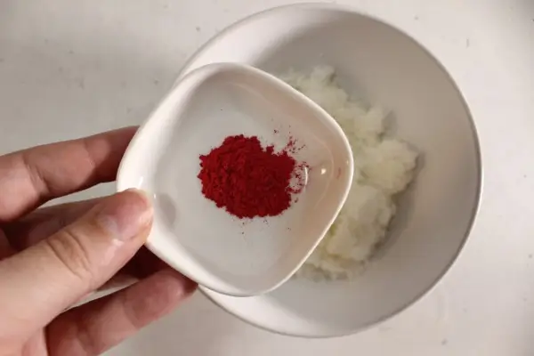 adding red mica powder to a bowl of white sugar scrub
