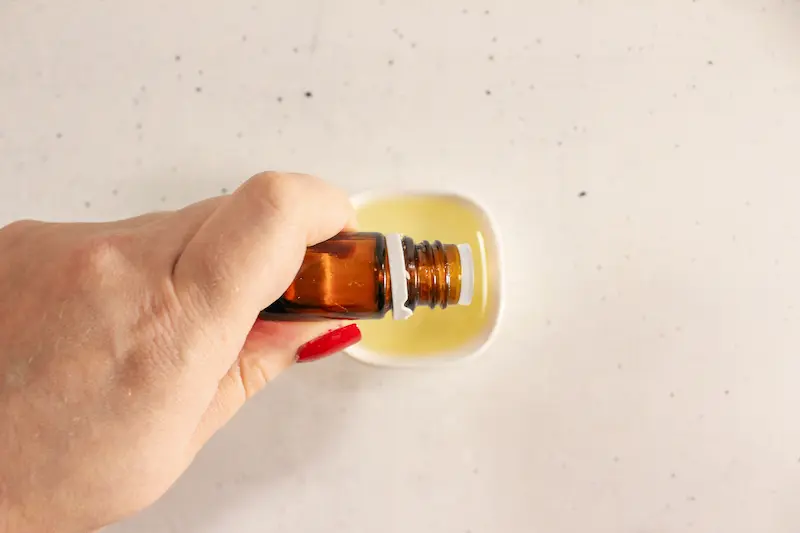 Rose Chocolate Bath Bomb Recipe 16 woman's hand holding a bottle of essential oil over a bowl of carrier oil to make chocolate rose bath bombs