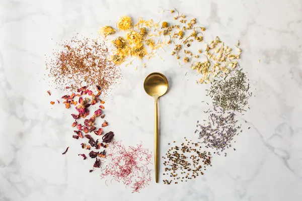 Calming Bedtime Tea Recipes For Sleep 13 dried herbal teas in a circle around a gold spoon