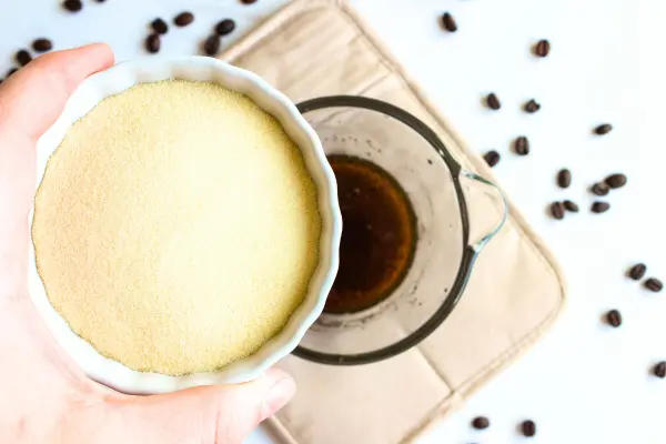 Under Eye Coffee Patches DIY Recipe 18 a bowl of coffee mixture and a hand holding a bowl of gelatin over it for making diy coffee eye patches