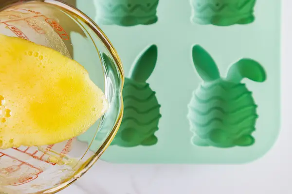 an easter bunny silicone soap mold with yellow soap mixture being poured into it