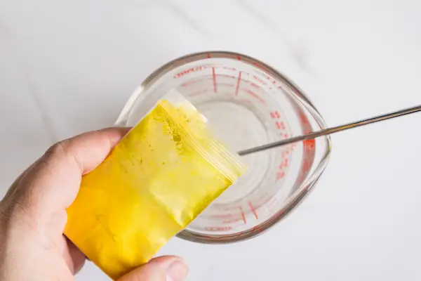 a pyrex measuring cup containing melted soap base and a woman's hand adding yellow mica powder to the mixture for making easter bunny soaps