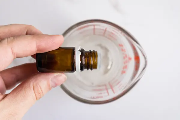 a pyrex measuring cup with a woman's hand adding drops of essential oils to the soap base for making easter bunny soaps