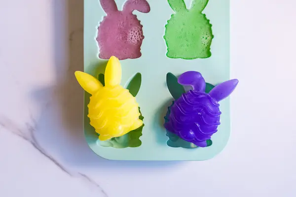 an easter bunny silicone soap mold filled with colored soap mixture and 2 of the soaps popped out of the mod