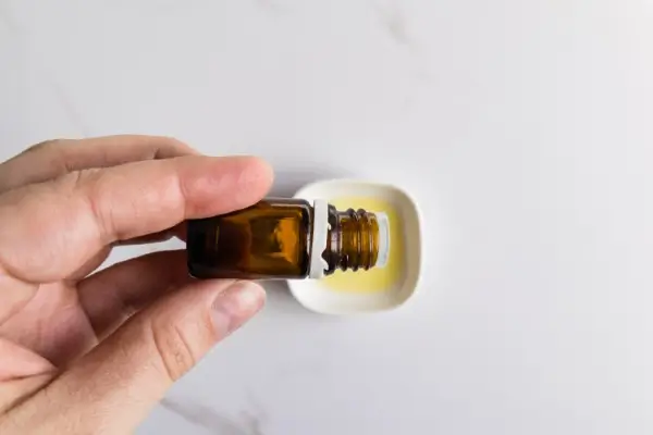 Easter Egg Bath Bombs Recipe 14 a bowl of almond oil and a hand adding drops from an essential oil bottle for making easter egg bath bombs