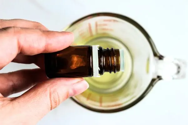 Lavender Tallow Oatmeal Face Scrub Recipe 19 a glass measuring cup with melted tallow and a hand holding a bottle of essential oil over it